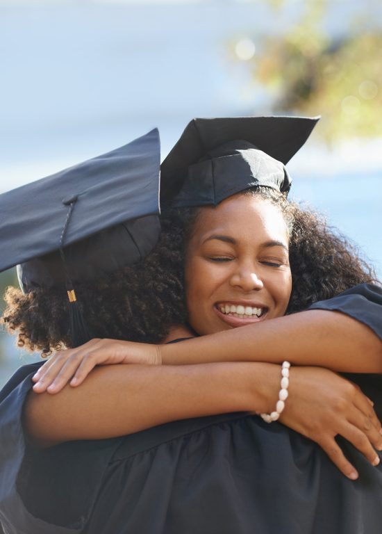 Woman in graduation clothing hugs a fellow student
